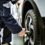 Close up of unrecognizable auto repairman using socket wrench while changing wheel and tire in a workshop.